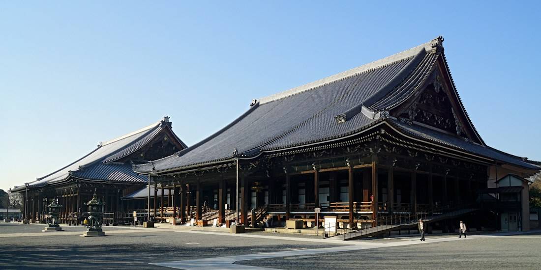 Vue panoramique des pavillons en bois sculpté du temple Nishi Hongan-ji, site classé à l'UNESCO à Kyoto, Japon, sous un ciel bleu clair.