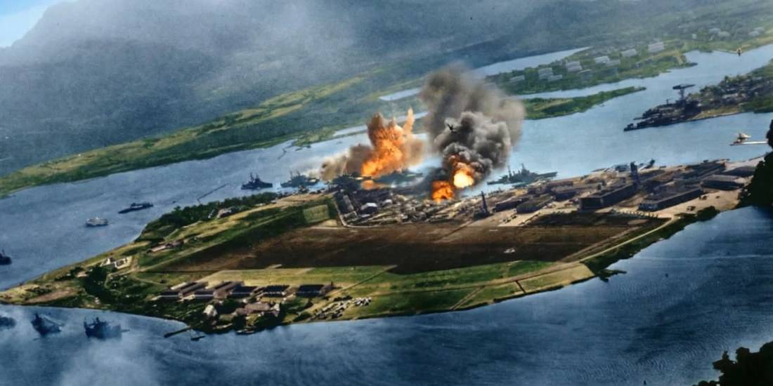 Photographie aérienne colorisée de l'attaque japonaise sur Pearl Harbor en 1941 montrant des explosions sur l'île de Ford et des navires de guerre américains sous les bombes.