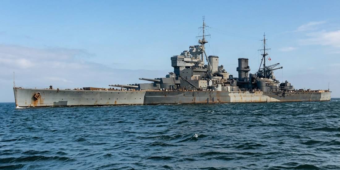 Photographie historique de profil du cuirassé britannique HMS Prince of Wales naviguant en mer en 1941, montrant ses tourelles de canon et son camouflage de la Seconde Guerre mondiale.