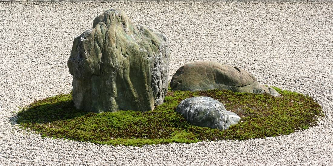 Gros plan sur une composition de rochers entourés de mousse verte sur un lit de gravier blanc ratissé dans le jardin zen du temple Ryoan-ji à Kyoto, Japon.