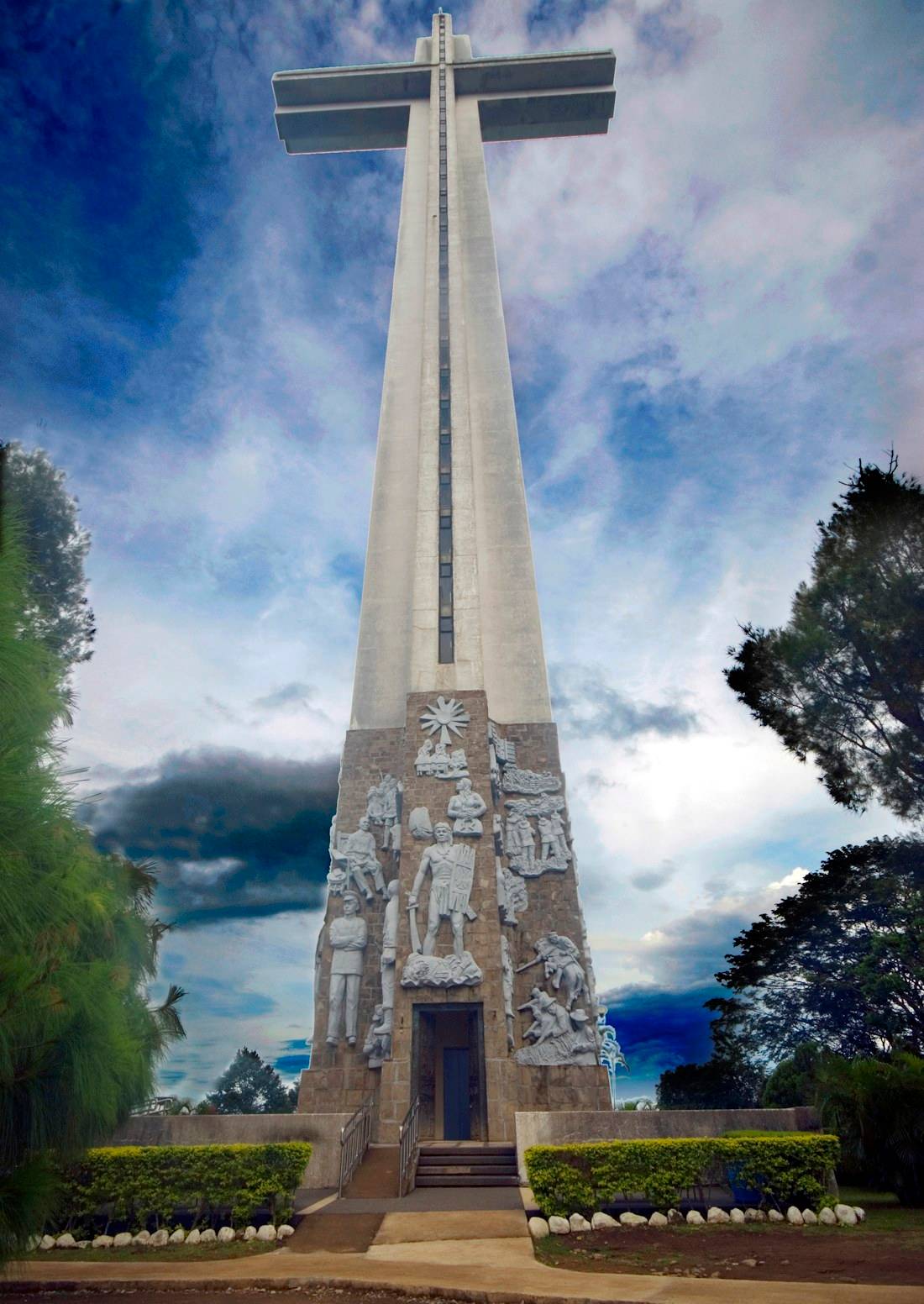 Mémorial national au sommet du Mont Samat, Sanctuaire de la Valeur à Bataan, Philippines, avec des bas-reliefs sculptés à la base sous un ciel nuageux.