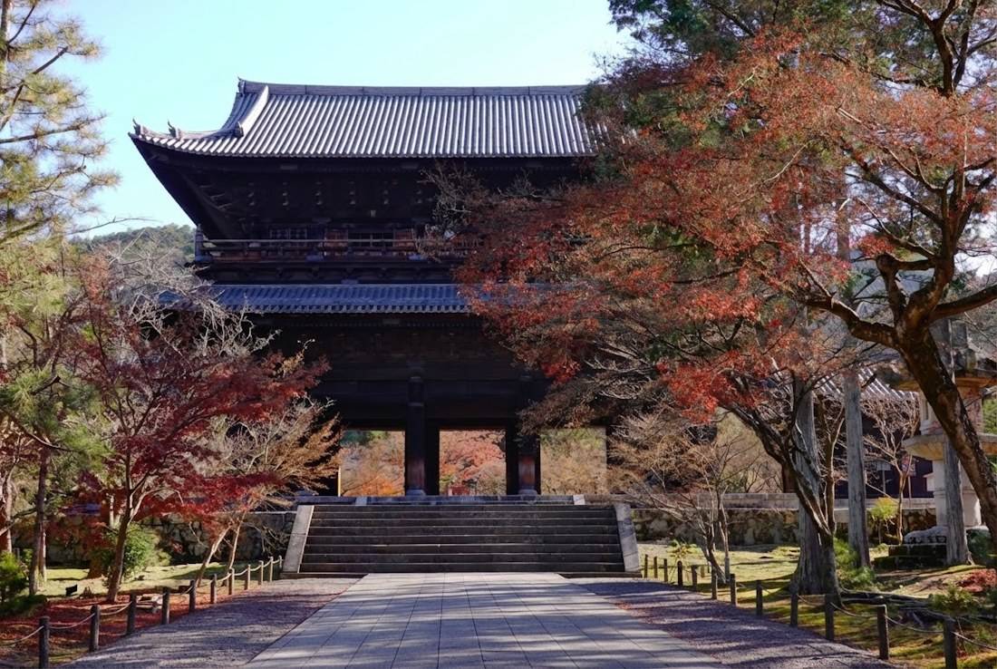 Porte Sanmon monumentale du temple Nanzen-ji à Kyoto entourée d'érables aux couleurs d'automne sous un ciel bleu.