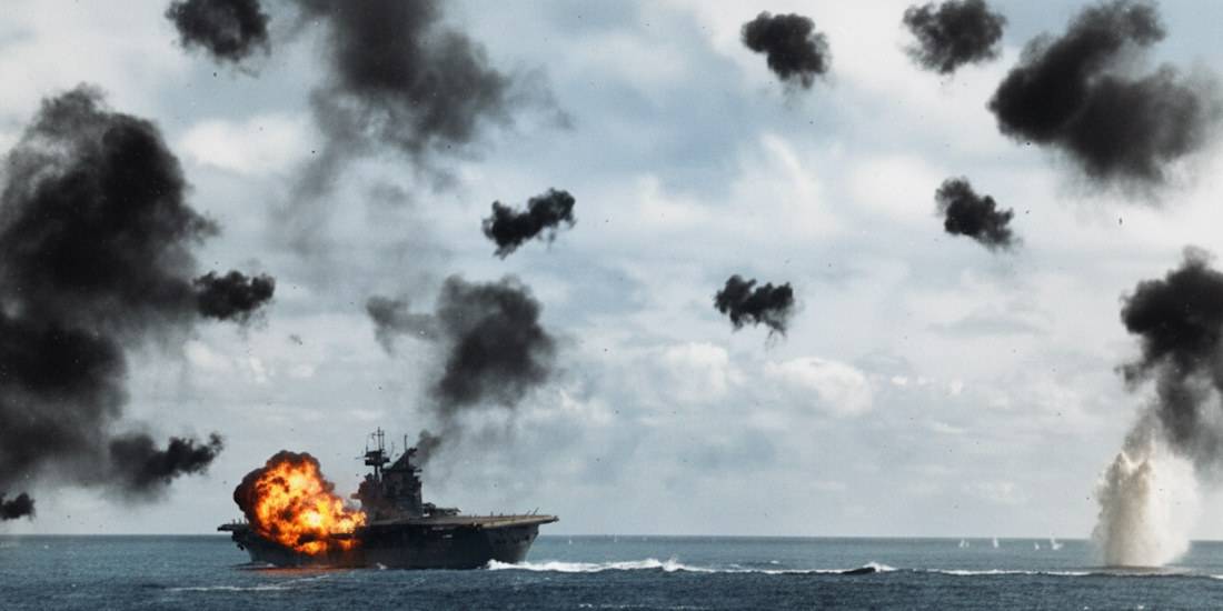 Porte-avions USS Yorktown (CV-5) sous le feu des attaques japonaises lors de la bataille de Midway en 1942, avec explosions de DCA et panaches de fumée noire dans le ciel.