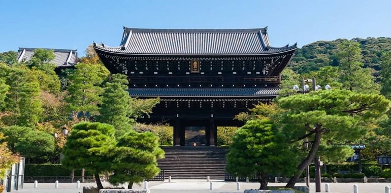Porte Sanmon monumentale en bois du temple bouddhiste Chion-in à Kyoto, Japon, entourée de pins sculptés sous un ciel bleu clair.