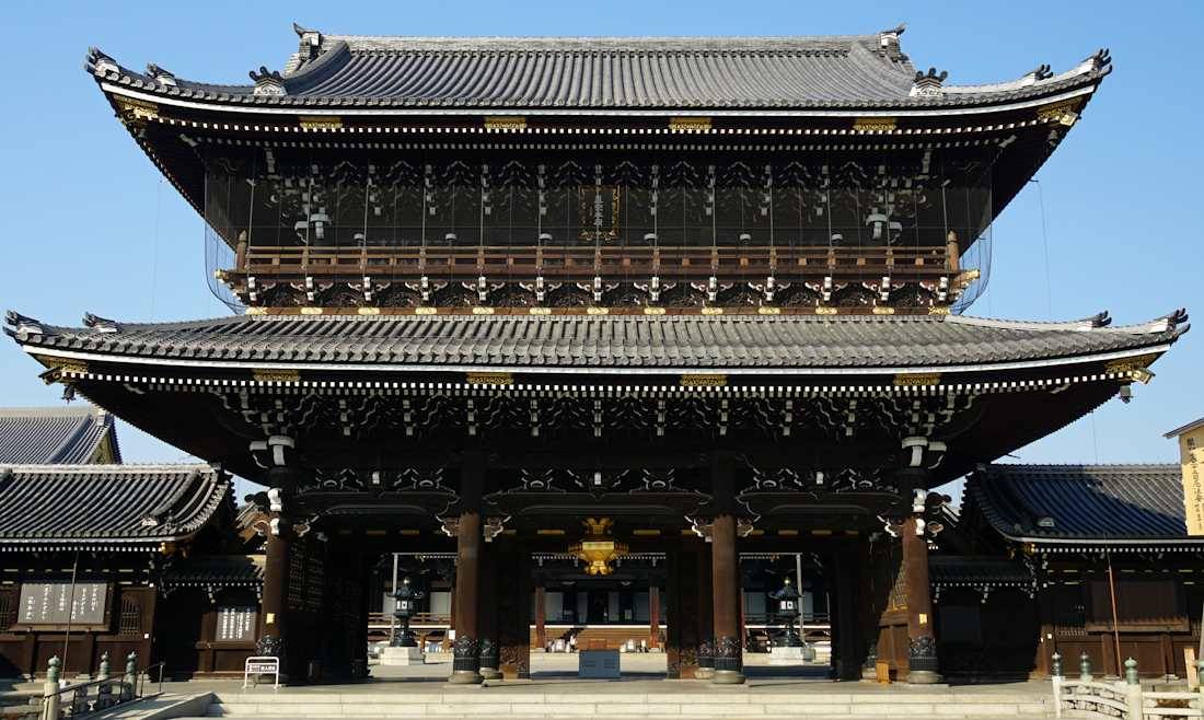 Porte Goei-do monumentale du temple bouddhiste Higashi Hongan-ji à Kyoto, Japon, montrant l'architecture traditionnelle en bois sculpté sous un ciel bleu.