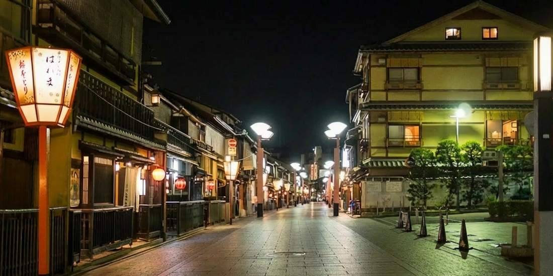 Vue nocturne de la rue Hanamikoji dans le quartier de Gion à Kyoto, montrant des lanternes traditionnelles éclairées et l'architecture classique des machiya japonaises sous un ciel de nuit.