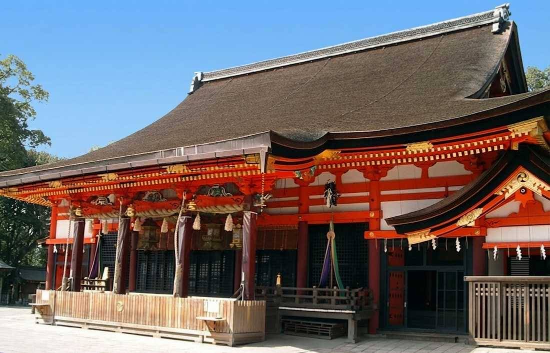 Vue rapprochée de l'architecture traditionnelle en bois rouge et du toit de chaume du bâtiment principal Honden-Haiden au sanctuaire Yasaka-jinja à Kyoto, Japon.