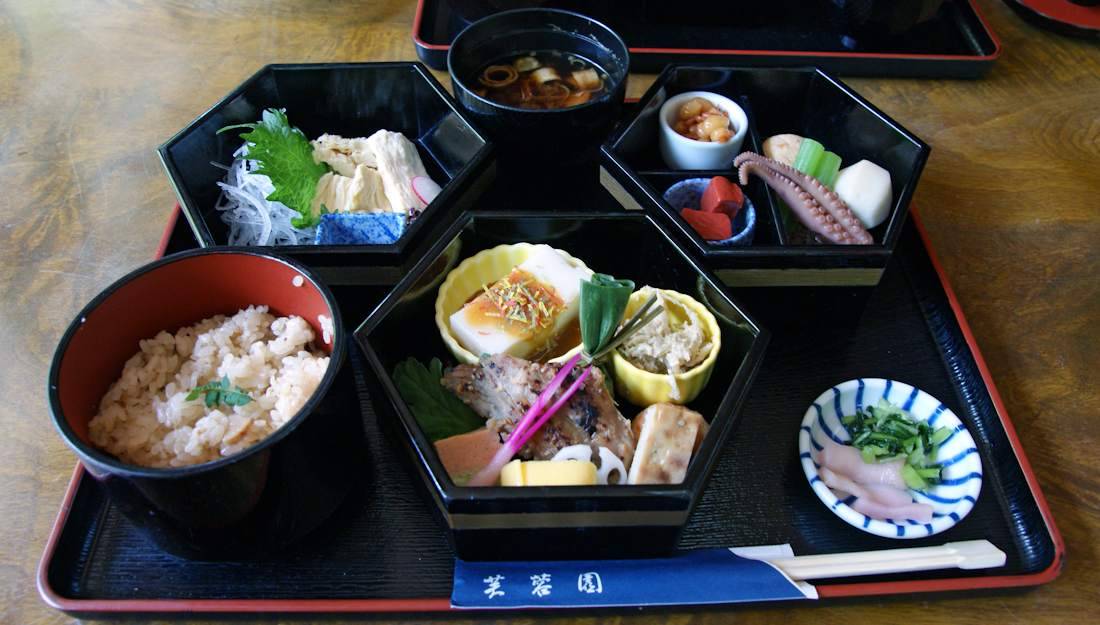 Repas traditionnel japonais kaiseki servi dans des boîtes laquées noires à Gion, Kyoto, comprenant du riz, de la soupe miso, du tofu et des spécialités de saison.