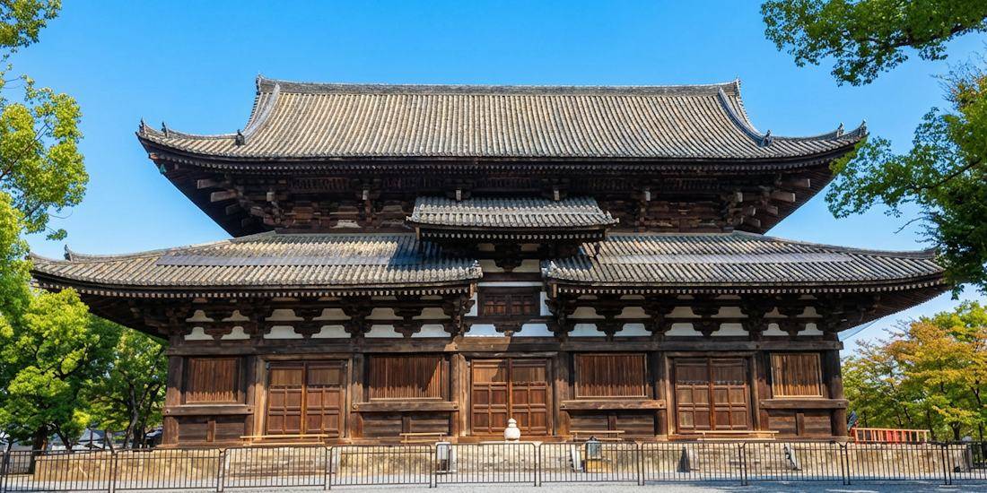 Façade en bois du Kondo, le bâtiment principal du temple To-ji à Kyoto, classé au patrimoine mondial de l'UNESCO, sous un ciel bleu avec des arbres verdoyants.