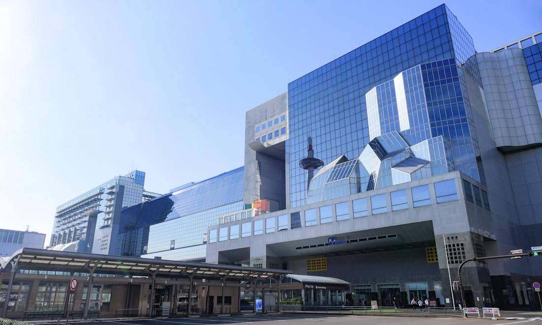 Façade moderne en verre de la gare de Kyoto au Japon avec le reflet de la tour de Kyoto sous un ciel bleu.