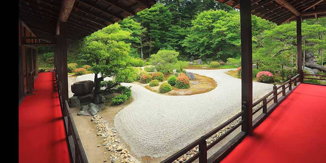 Jardin sec karesansui du temple Manshu-in à Kyoto avec sable ratissé, azalées en fleurs et tapis rouge sur la véranda en bois.