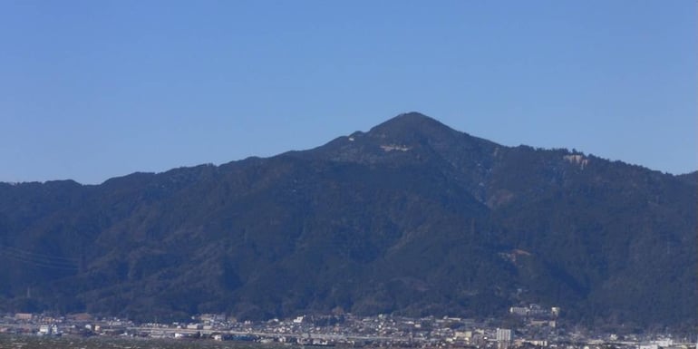 Vue panoramique du mont Hiei dominant la ville depuis les rives du lac Biwa au Japon sous un ciel bleu clair.