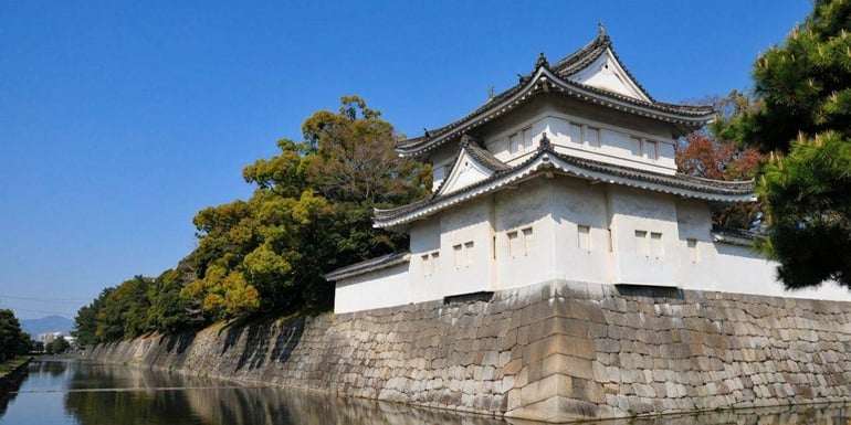 Vue extérieure du château de Nijo à Kyoto, Japon, montrant une tour de guet blanche (yagura) sur des murs en pierre massifs bordant les douves sous un ciel bleu clair.