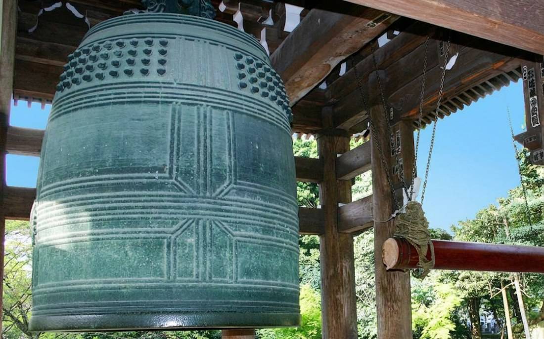 Grande cloche de bronze Ogane du temple bouddhiste Chion-in à Kyoto, Japon, suspendue dans son beffroi en bois traditionnel sous un ciel bleu.