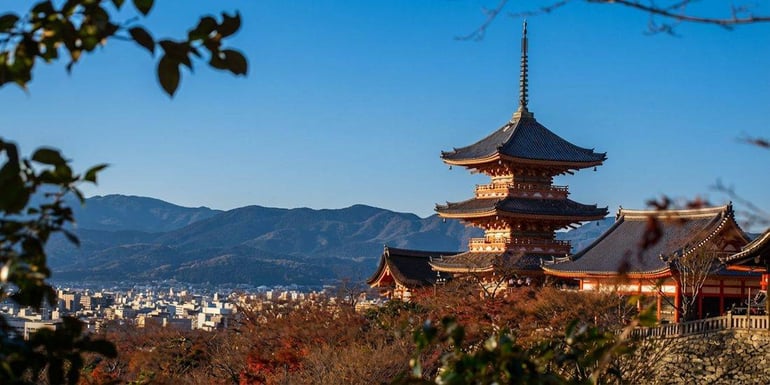 Pagode à trois étages du temple Kiyomizu-dera surplombant la ville de Kyoto au Japon sous un ciel bleu clair avec les montagnes en arrière-plan.