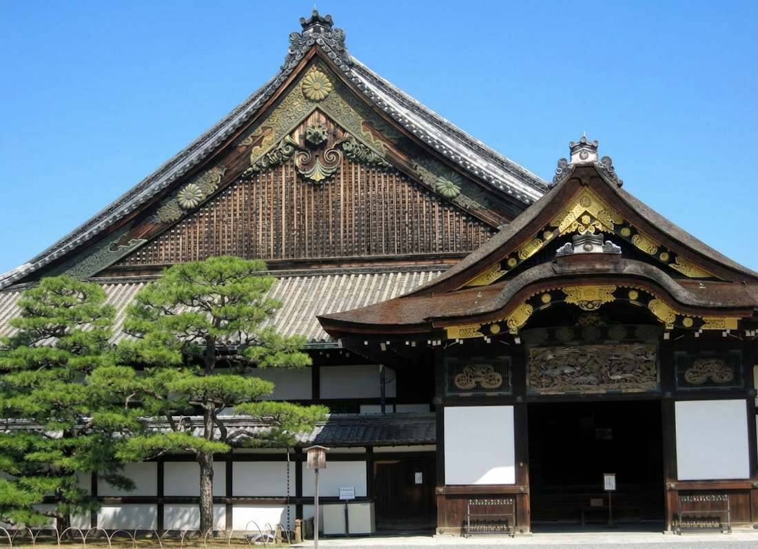 Entrée principale du Palais Ninomaru au château de Nijo à Kyoto, montrant l'architecture traditionnelle japonaise en bois, les sculptures dorées et le toit en écorce de cyprès sous un ciel bleu.