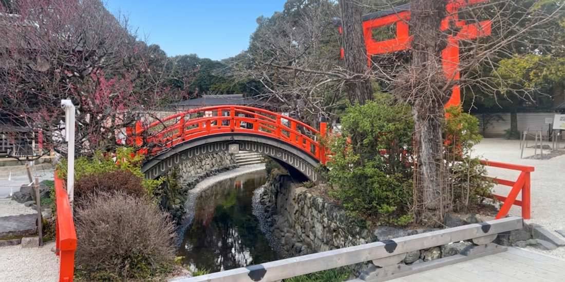 Pont Taikobashi rouge arqué traversant un ruisseau au sanctuaire Shimogamo-jinja à Kyoto, Japon, entouré de végétation et d'un portail torii.