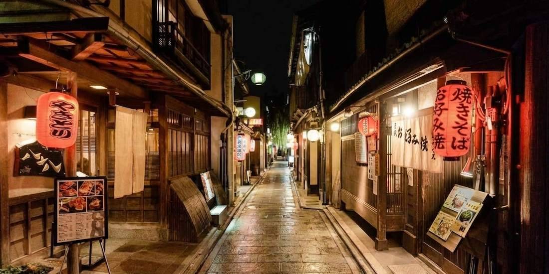 Ruelle traditionnelle Ponto-chō à Kyoto de nuit avec lanternes rouges allumées, restaurants typiques en bois et pavés luisants au Japon.