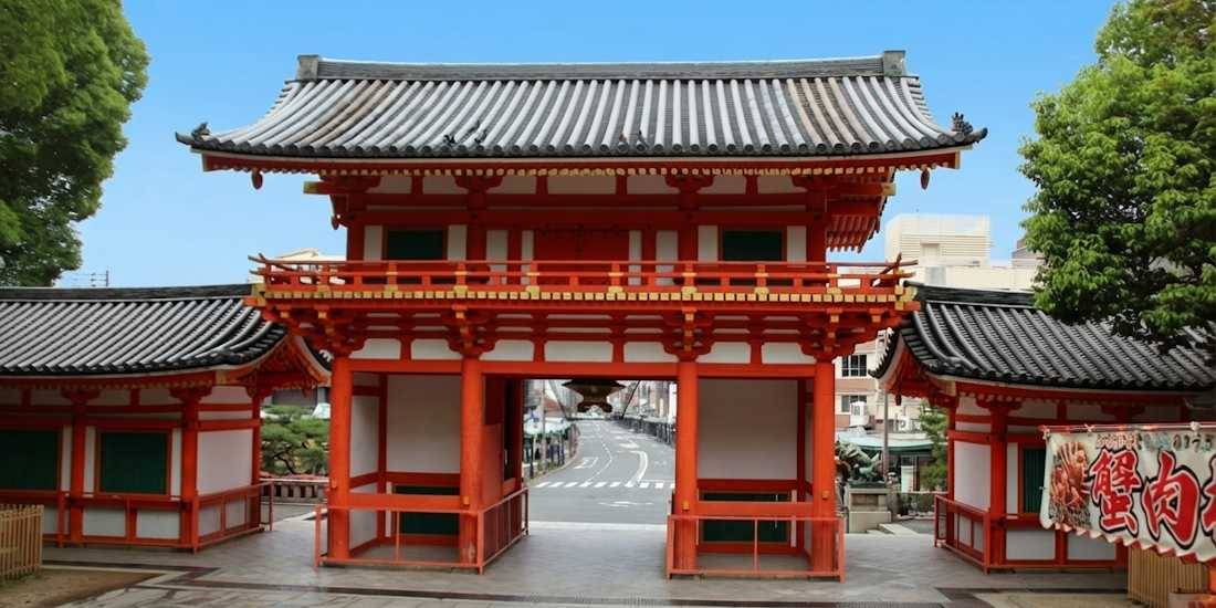 Porte Romon vermillon à deux étages du sanctuaire Yasaka-jinja à Kyoto, Japon, vue de l'intérieur vers la rue Shijo sous un ciel bleu.