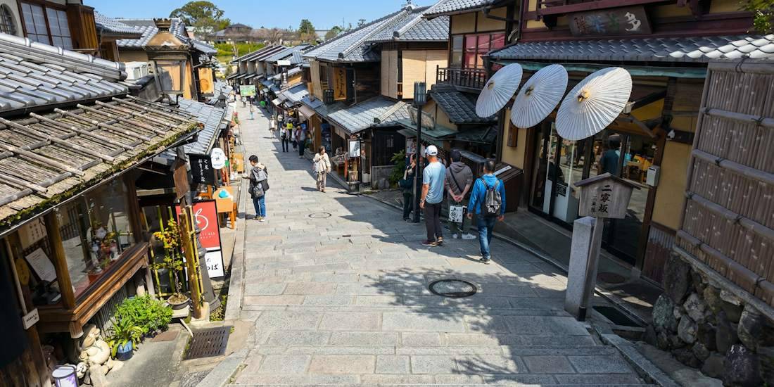 Vue en plongée de la rue pavée historique de Sannenzaka à Kyoto, bordée de maisons traditionnelles japonaises en bois, de boutiques d'artisanat et de passants sous un ciel bleu clair près du temple Kiyomizu-dera.