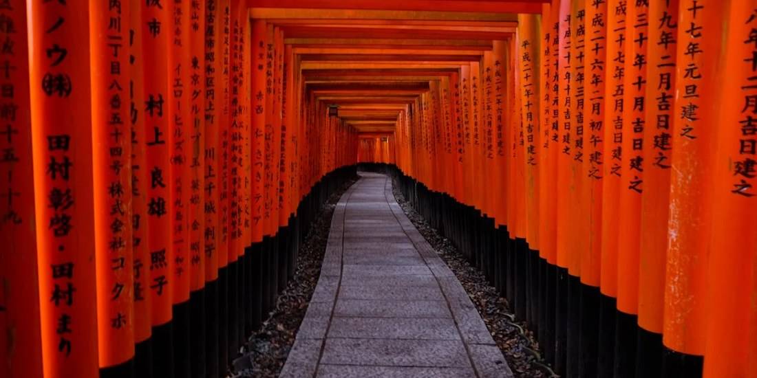 Tunnel de portails torii vermillon Senbon Torii au sanctuaire Fushimi Inari-taisha à Kyoto, Japon, avec calligraphies japonaises noires sur les piliers en bois.