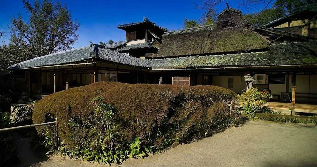 Vue extérieure du temple Shisen-do à Kyoto avec son toit de chaume traditionnel, ses jardins zen sculptés et son architecture japonaise historique sous un ciel bleu.