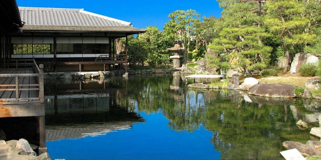 Jardin japonais Shosei-en avec pavillon traditionnel en bois et étang reflétant le ciel bleu à Kyoto, près du temple Higashi Hongan-ji.