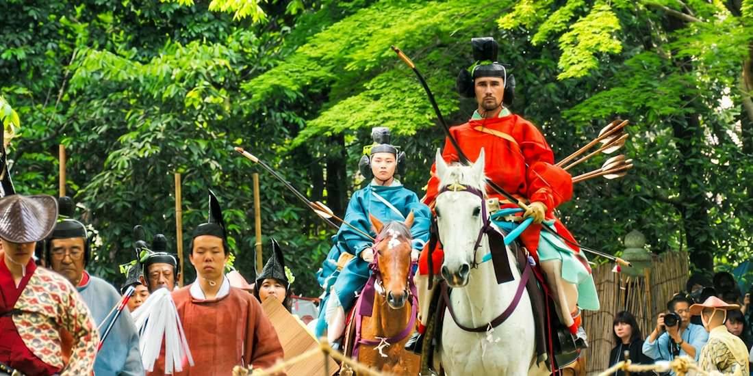 Archer en costume traditionnel rouge chevauchant un cheval blanc lors du rituel de tir à l'arc japonais Yabusame Shinji au sanctuaire Shimogamo-jinja à Kyoto.