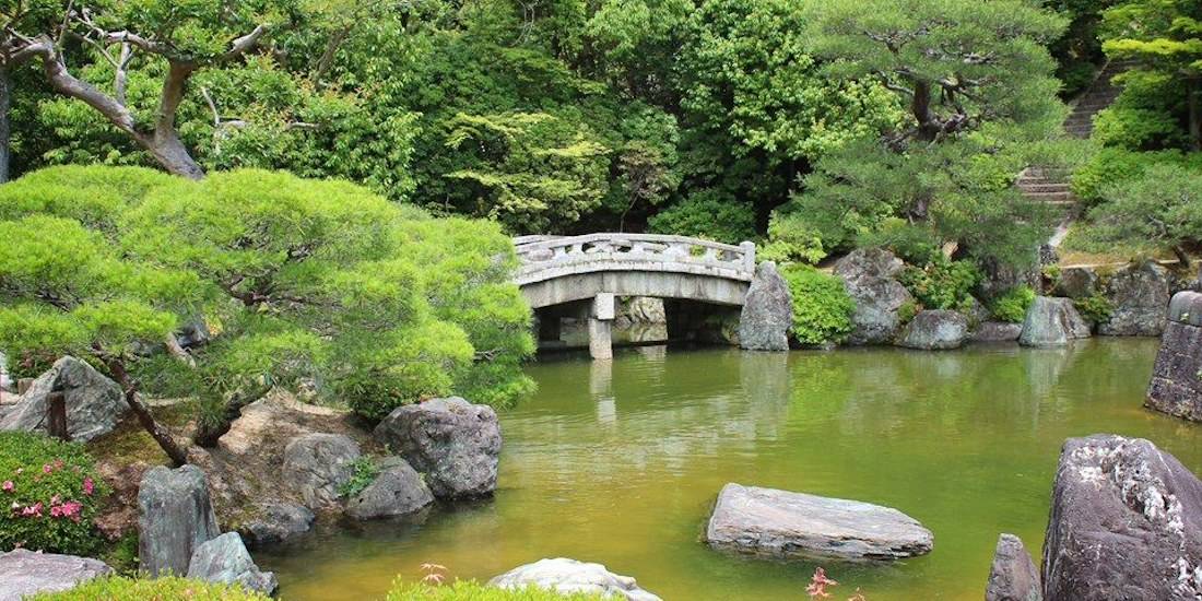 Pont en pierre traditionnel traversant un étang paisible dans le jardin Yuzen-en du temple Chion-in à Kyoto, Japon, entouré de pins sculptés et d'une végétation luxuriante.