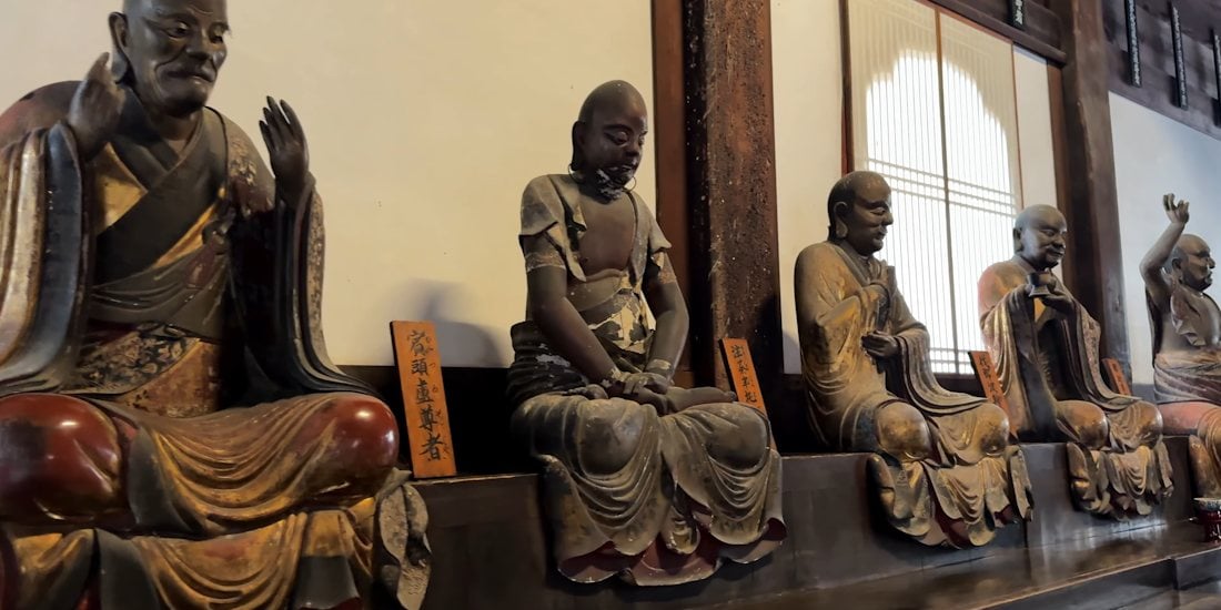 Rangée de statues d'Arhats en bois sculpté dans le bâtiment Daihoden du temple Manpuku-ji à Uji, Kyoto, montrant des disciples de Bouddha avec des expressions et des postures uniques.