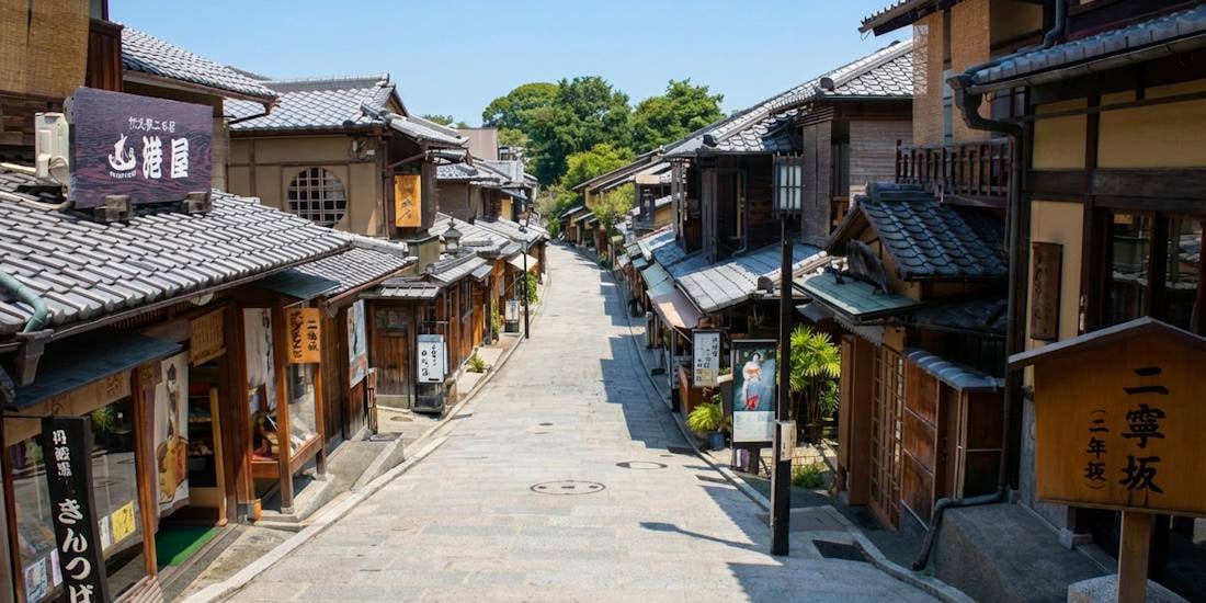 Rue pavée traditionnelle de Sannenzaka dans le quartier historique de Higashiyama à Kyoto, Japon, bordée de maisons en bois anciennes sous un ciel bleu.