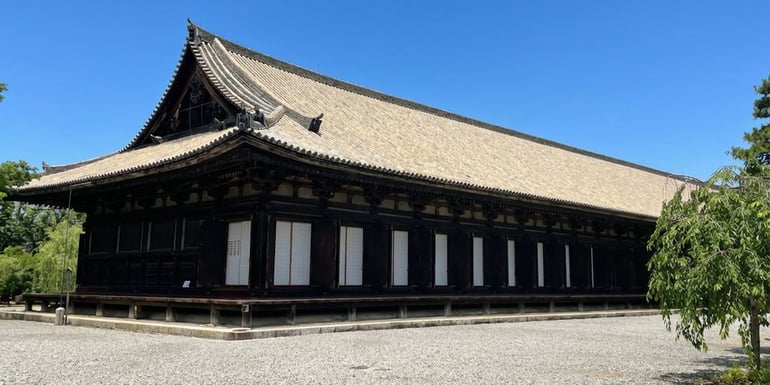 Vue extérieure du temple Sanjūsangen-dō à Kyoto, Japon, montrant l'architecture traditionnelle en bois du long pavillon principal sous un ciel bleu clair.