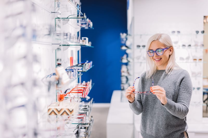 Woman wearing purple glasses as she browses eyeglass frames in an optical store
