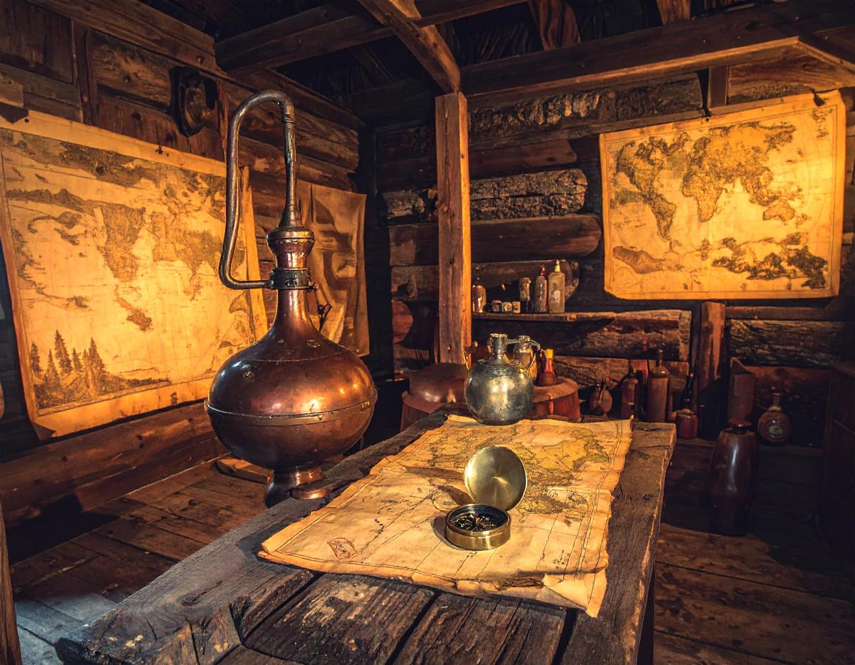 A copper alembic, brass compass and antique maps on a wooden table