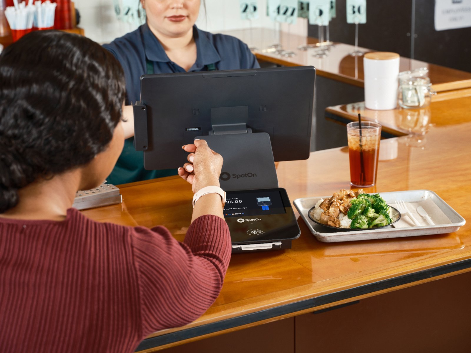 Guest tapping a smartwatch to pay on a SpotOn POS terminal at a counter-service restaurant