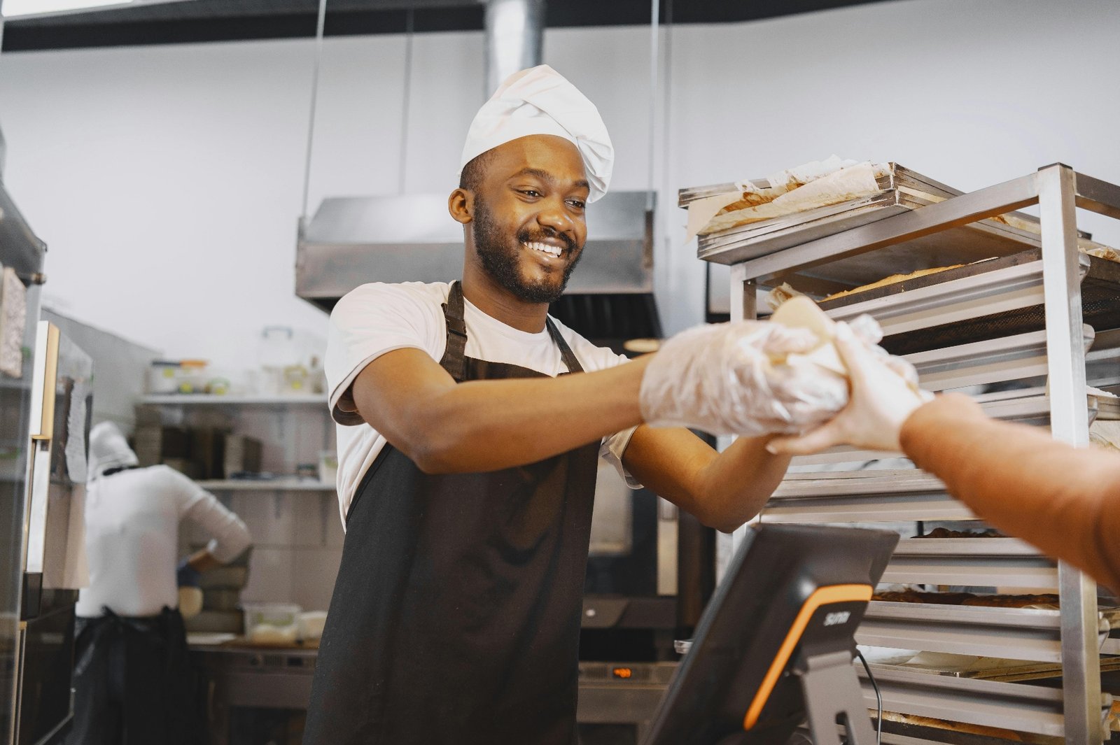 Smiling kitchen staff handing a takeout bag across the pickup counter