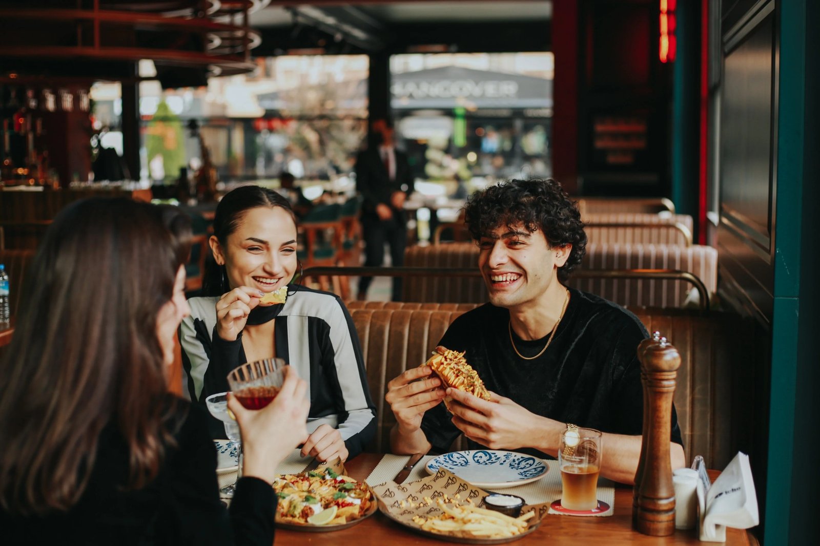 Three friends laughing and sharing food at a restaurant table, enjoying focused in-person service
