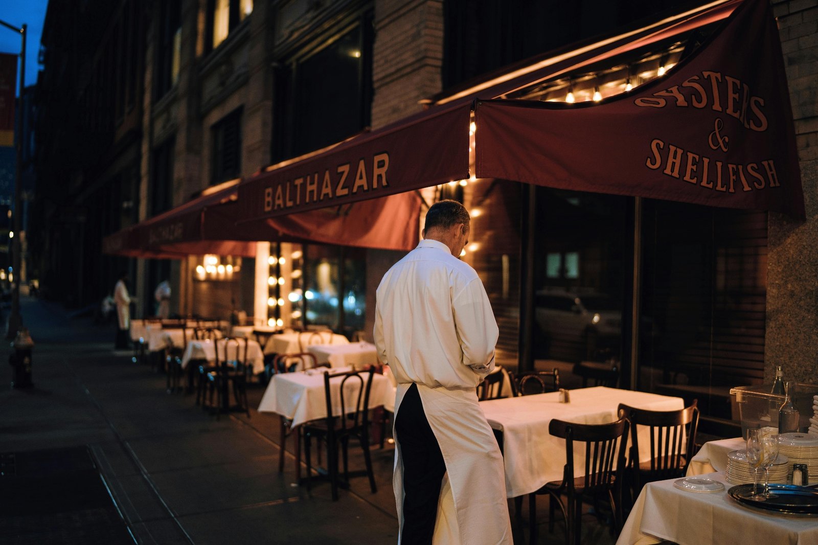 Lone waiter outside an empty restaurant at dusk