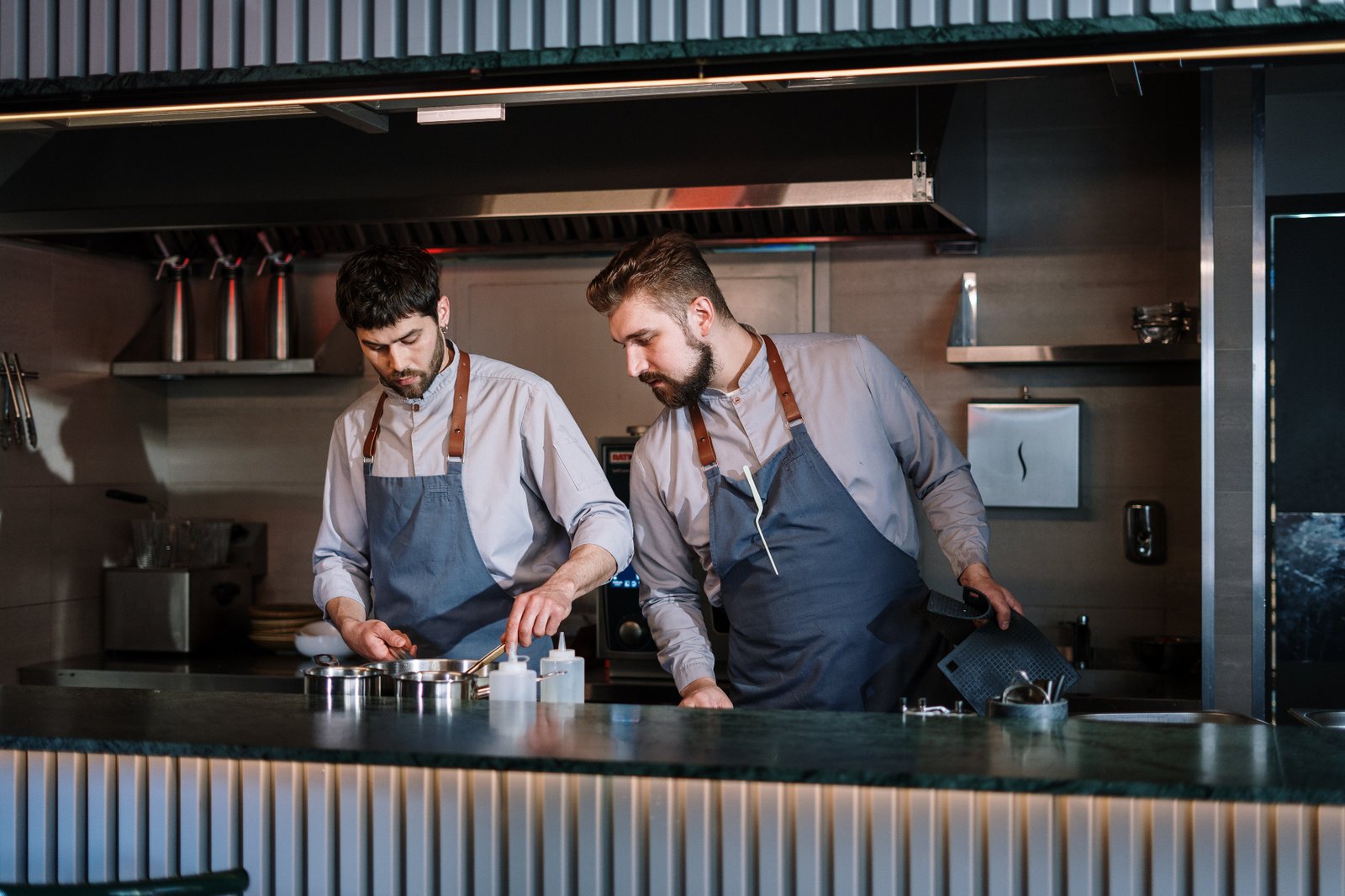 Two restaurant chefs collaborating on the line, reviewing prep and service data during a kitchen shift