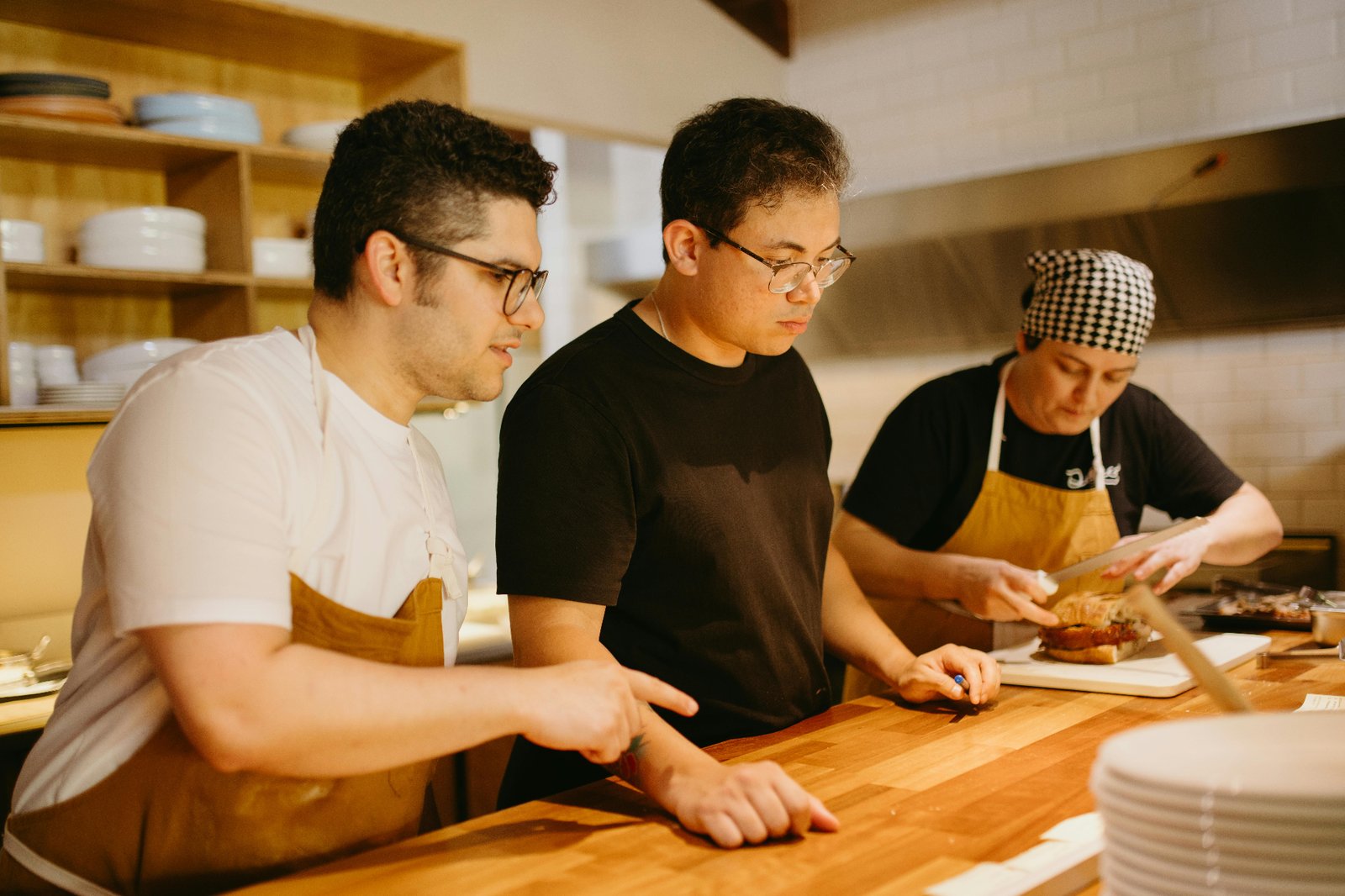 Head chef training two line cooks on plating standards and station setup in a full-service restaurant kitchen
