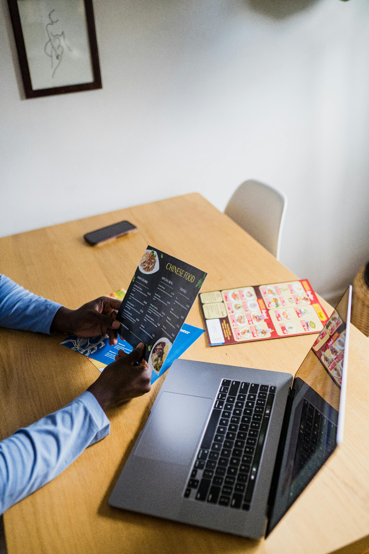 Restaurant operator reviewing a printed menu next to a laptop, evaluating phone ordering and voice AI options for the business.