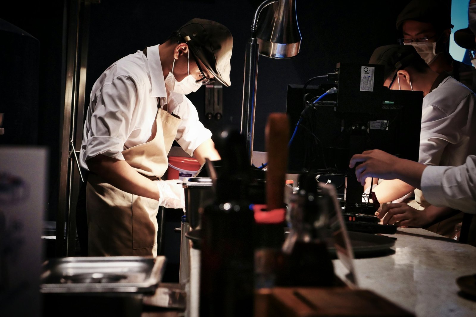 Chefs working in a dimly lit restaurant kitchen alongside a digital order monitor