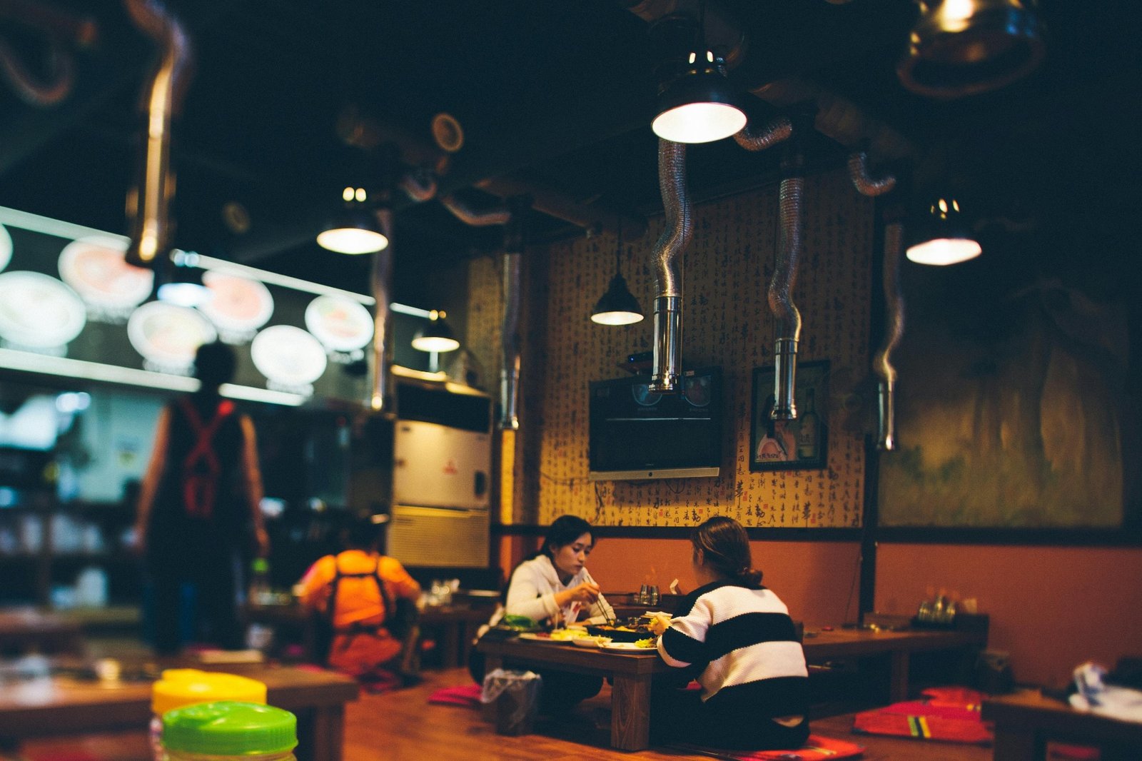 Warmly lit Asian restaurant interior with guests dining at a table while staff move through the dining room during service