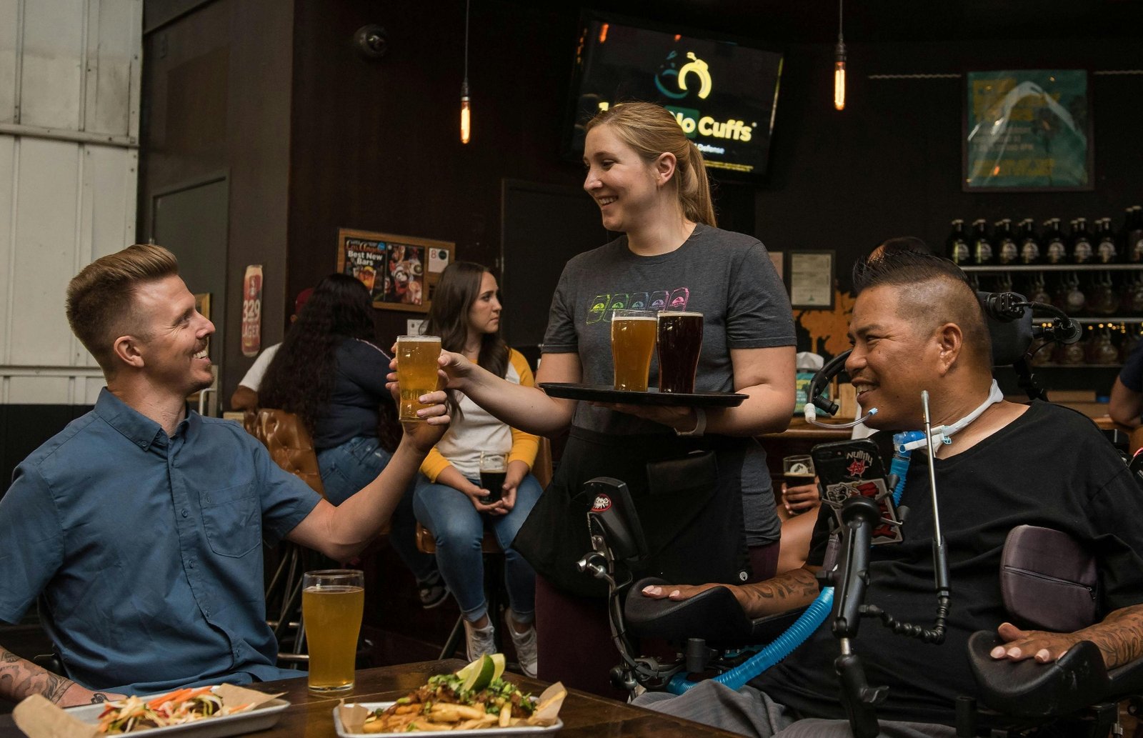 Smiling server delivering a tray of beer flights to guests at a busy independent restaurant, capturing every order to increase restaurant revenue
