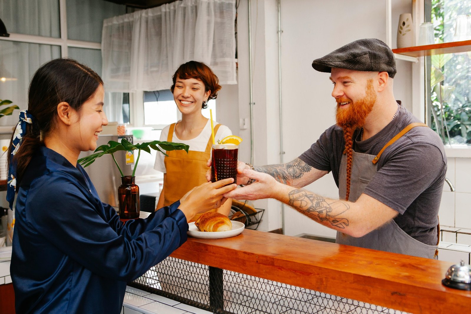 Smiling baristas handing a fresh drink to a happy customer at a cafe counter
