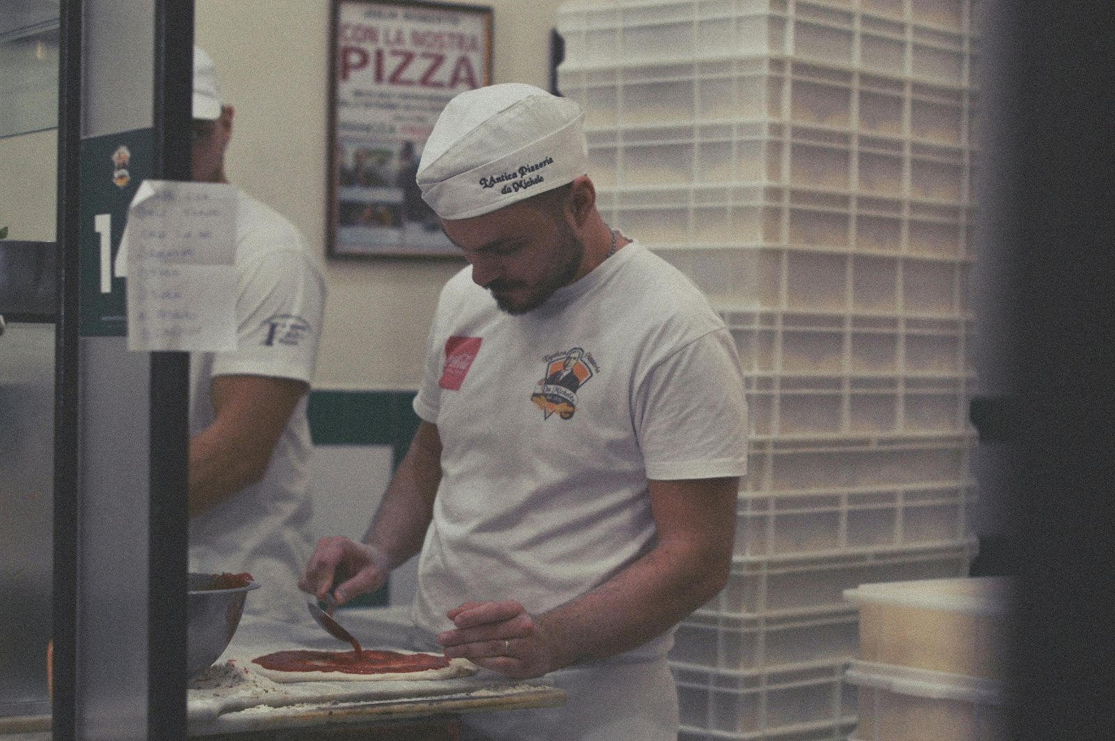 Italian pizzaiolo spreading San Marzano tomato sauce on hand-stretched pizza dough in a traditional pizzeria kitchen