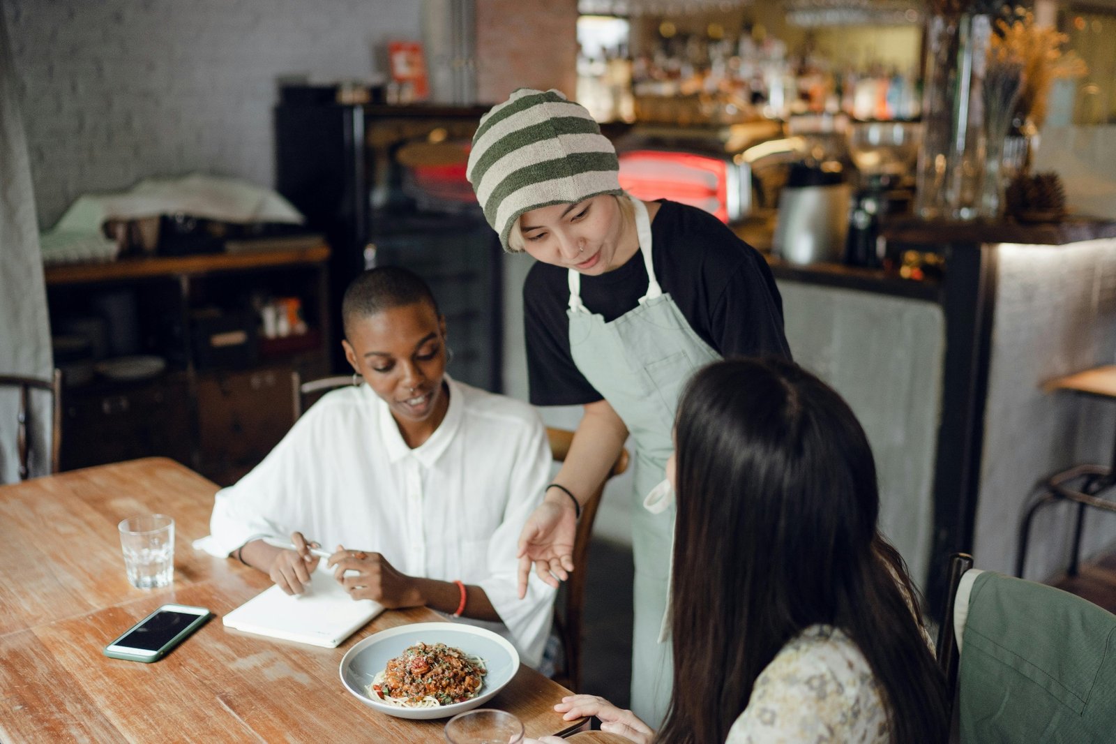 Front-of-house server taking a guest order tableside while training on menu knowledge and active listening in a casual dining restaurant