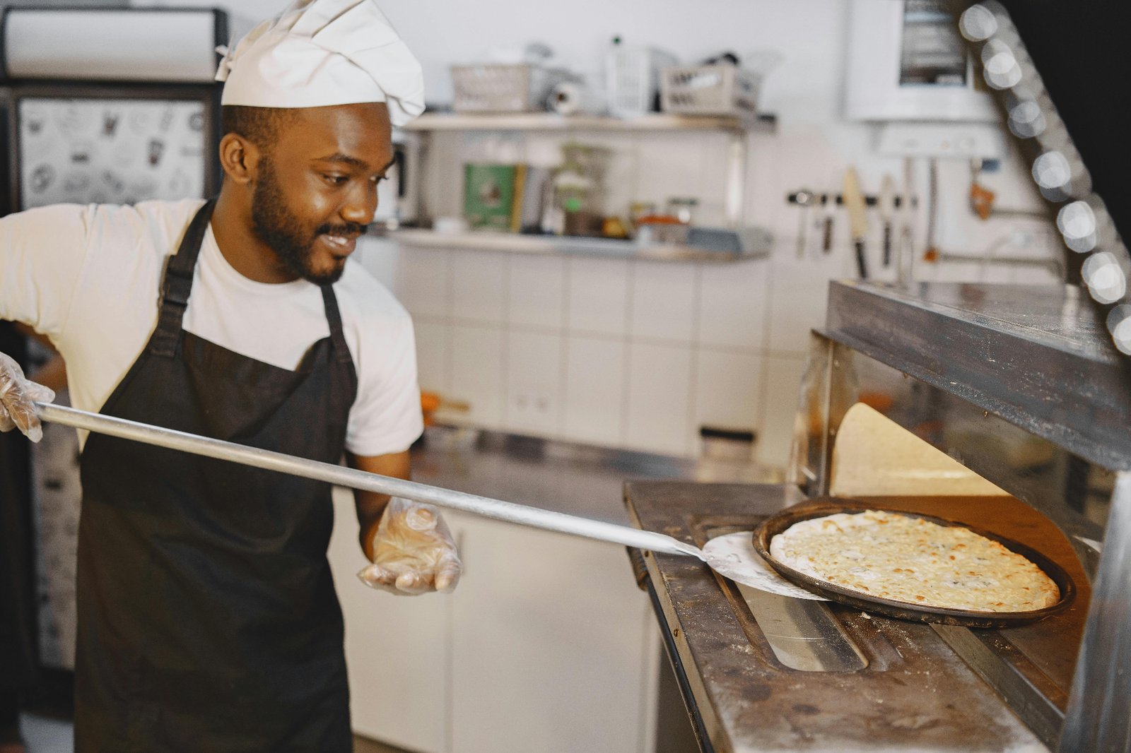 Pizzeria chef in apron pulling a freshly baked pizza out of the deck oven on a metal peel
