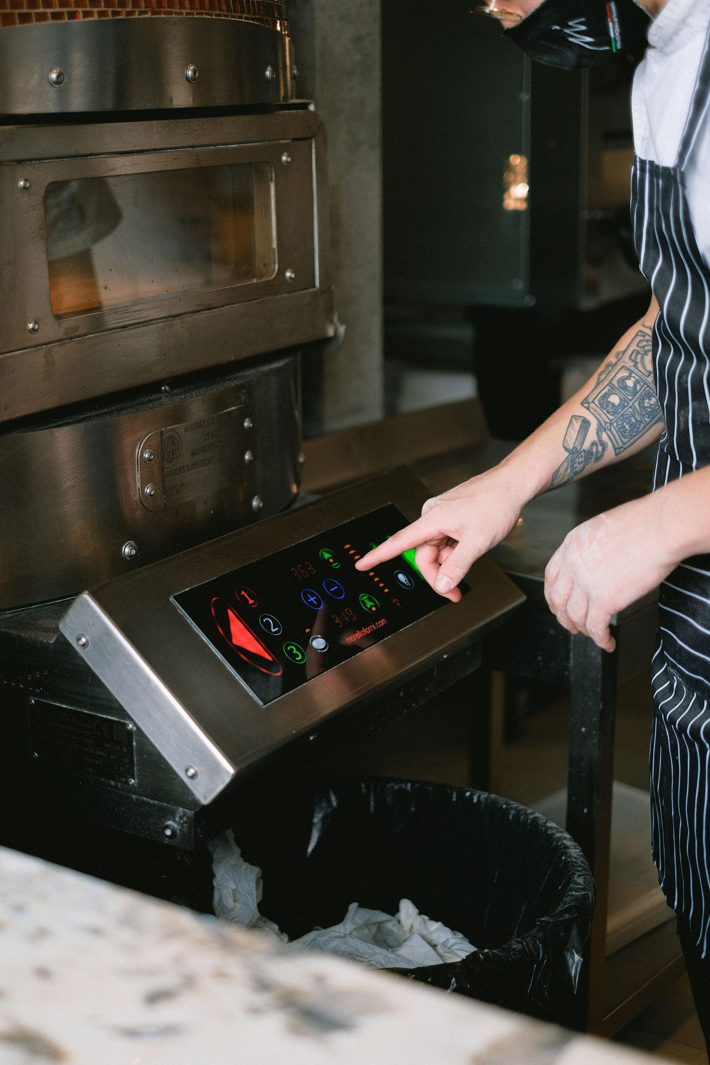 A busy commercial kitchen with digital kitchen display screens mounted above a prep station showing colorful order information, illustrating how a KDS routes tickets to the line.