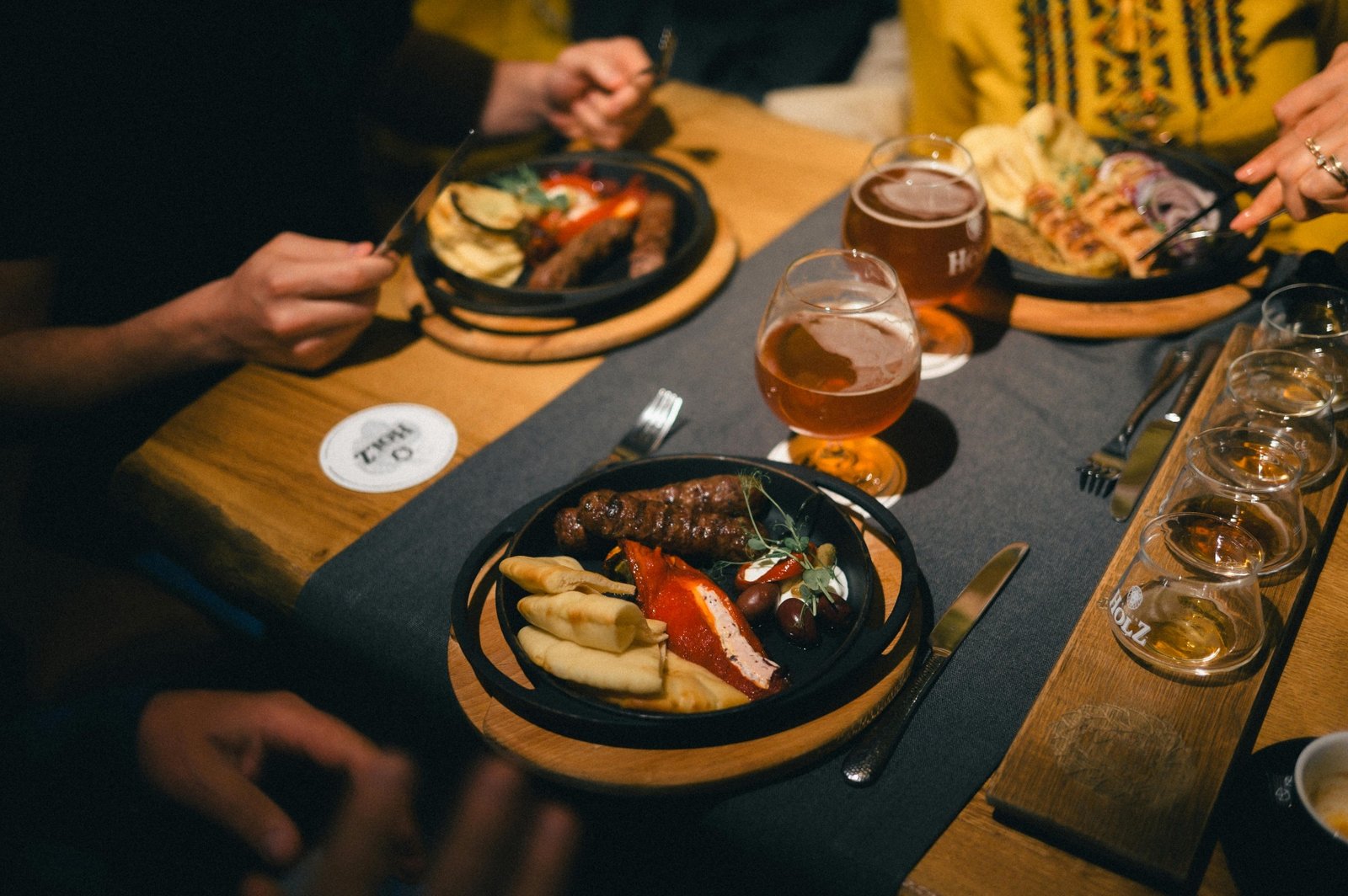 Friends sharing plates of grilled food and craft beer at a wooden restaurant table
